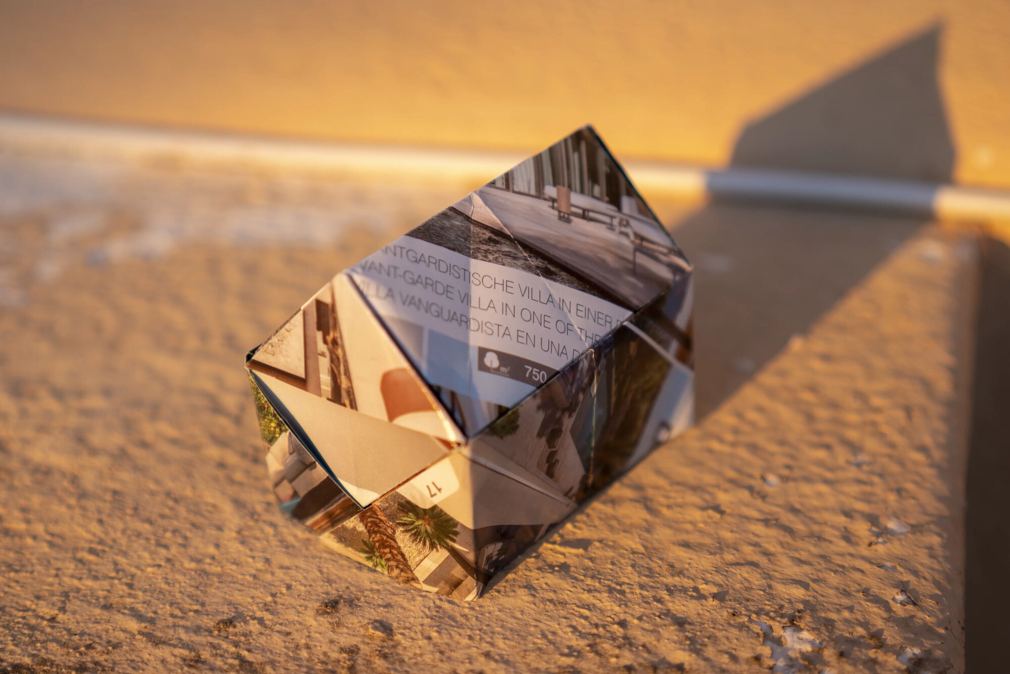 Origami house folded from a real-estate listing for an avant-garde villa, photographed on stone in evening light