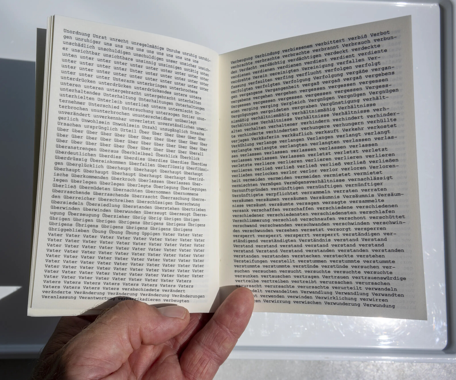 Another open spread, held in hand, with repeated blocks of words like 'unter' and 'Vater' stacked line after line